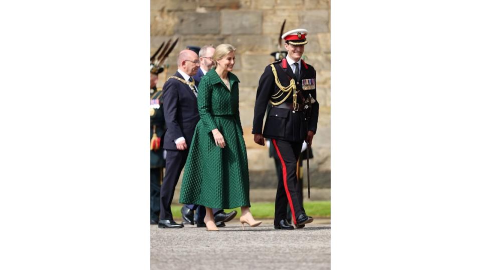 Sophie in green look walking with uniformed man 