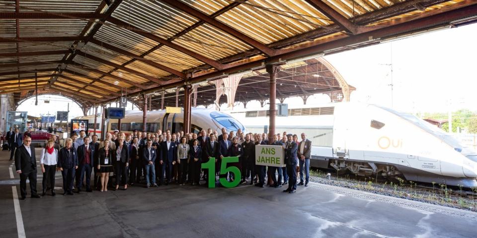People gathered at a terminal celebrating the partnership between DB and SNCF. The row pf people are holding a banner and a cutout of the number 15.