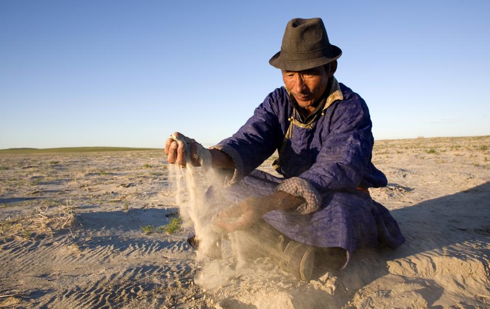 A photo of a Mongolian nomadic herder, running sand from a dry lake bed through his hands.