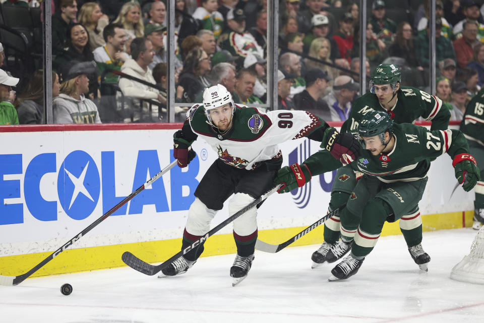 Arizona Coyotes defenseman J.J. Moser, left, skates with the puck as Minnesota Wild center Jacob Lucchini (27) and center Vinni Lettieri (10) defend during the first period of an NHL hockey game Tuesday, March 12, 2024, in St. Paul, Minn. (AP Photo/Matt Krohn)