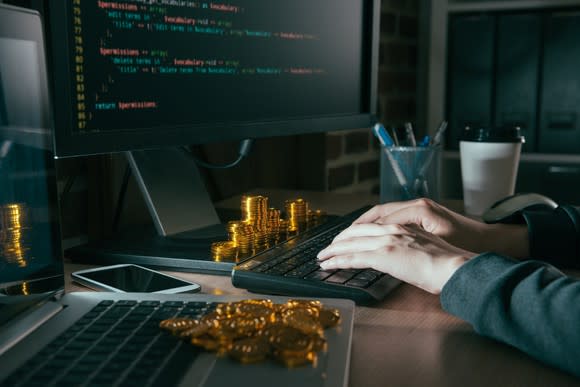 A programmer at a computer programming code next to piles of coins