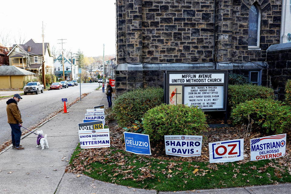 A man with a dog stands near campaign signs outside the Mifflin Avenue United Methodist Church during the 2022 US midterm elections on Nov. 8, 2022, in Pittsburgh.
