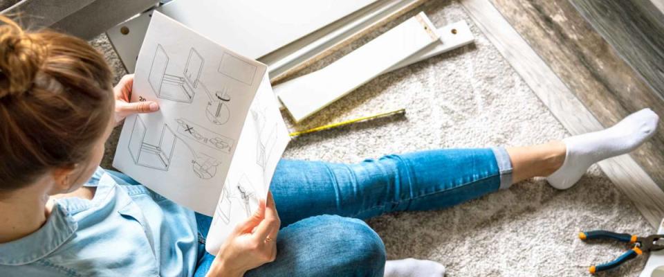 Concentrated young woman reading the instructions to assemble furniture at home in the living room