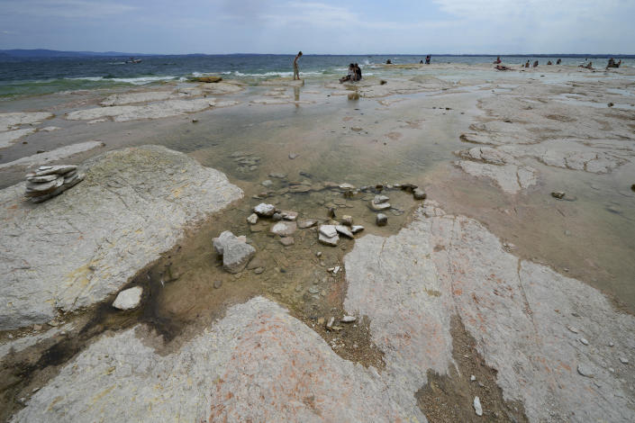 People relax on the peninsula of Sirmione, on Garda lake, Italy, Friday, Aug. 12, 2022. Lake Garda water level has dropped critically following severe drought resulting in rocks to emerge around the Sirmione Peninsula. (AP Photo/Antonio Calanni)
