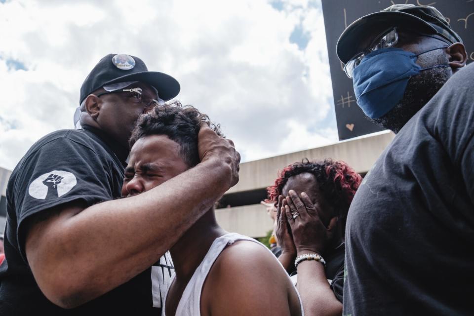 A minister holds a young boy who is crying while a woman nearby covers her face.