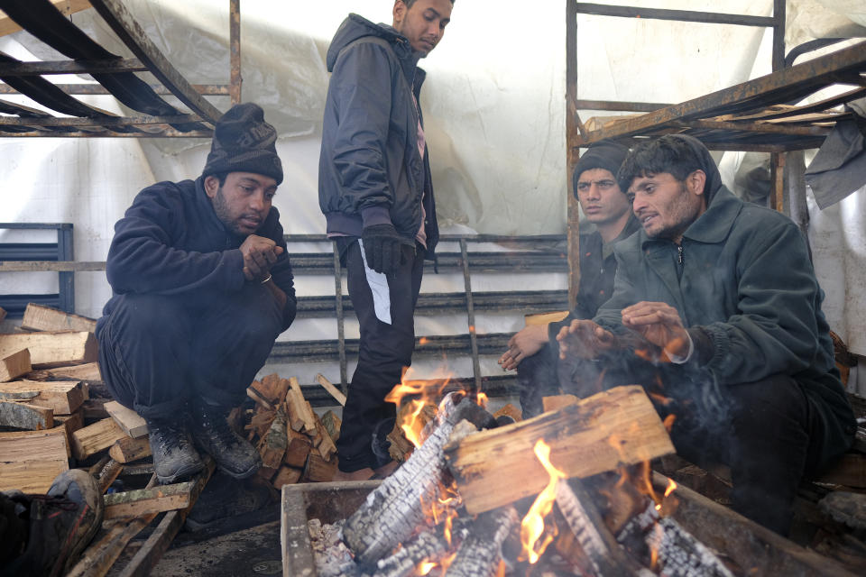 Migrants warm themselves around a fire in a makeshift tent at the Lipa camp, outside Bihac, Bosnia, Friday, Jan. 8, 2021. A fresh spate of snowy and very cold winter weather on has brought more misery for hundreds of migrants who have been stuck for days in a burnt out camp in northwest Bosnia waiting for heating and other facilities. (AP Photo/Kemal Softic)