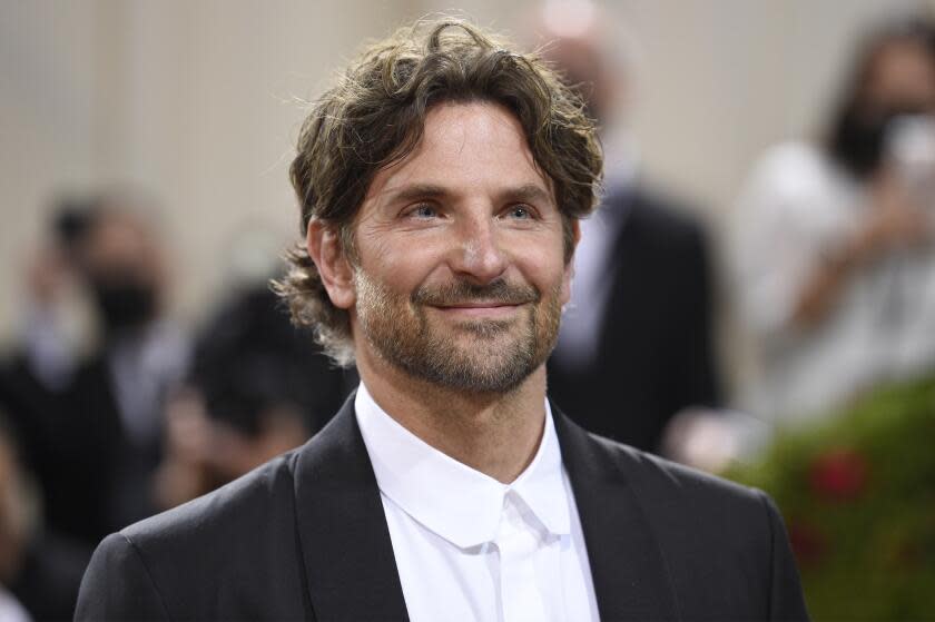 A man with long hair and and a short beard smiles while wearing a tuxedo