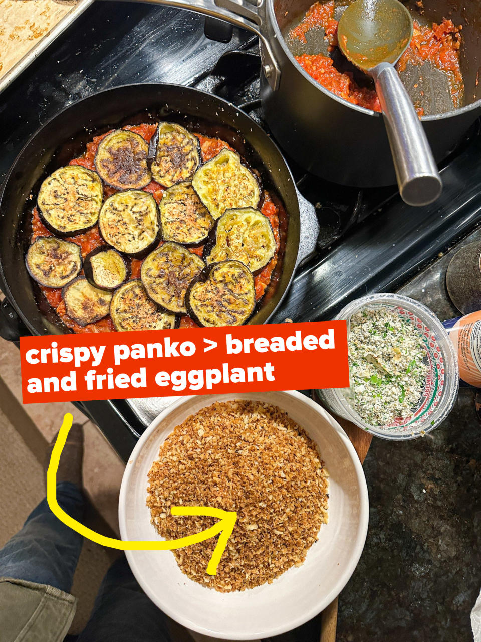 Assembling the eggplant Parm: Skillet with eggplant and sauce, bread crumbs, and Parmesan cheese next to it