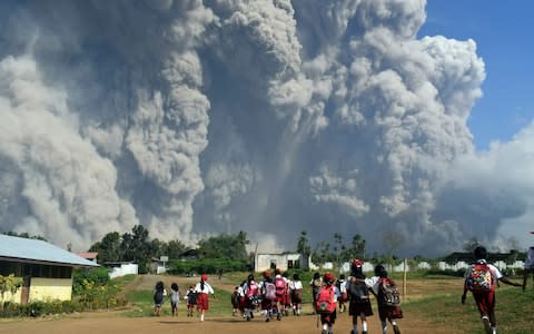 School children walk as Mount Sinabung erupts in Karo, North Sumatra, Indonesia, Monday, Feb. 19, 2018 - Credit: Sarianto/AP