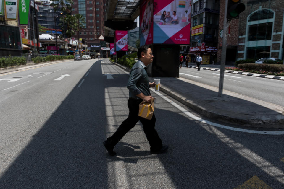 An office worker with takeout food crosses the street in Kuala Lumpur's Bukit Bintang area on 18 March 2020, the first day of the Movement Control Order. (PHOTO: Fadza Ishak for Yahoo Malaysia)