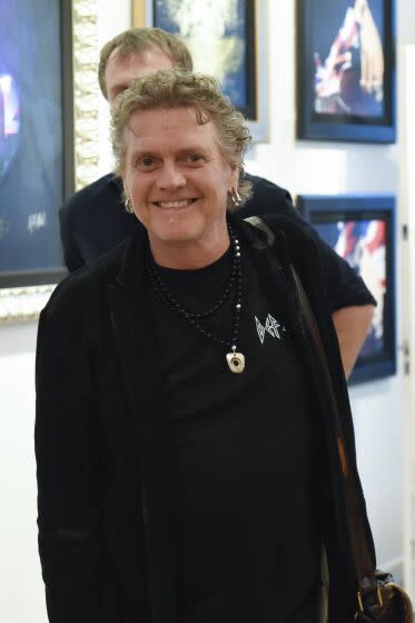 A man with short and curly gray hair in a black shirt and jacket smiling