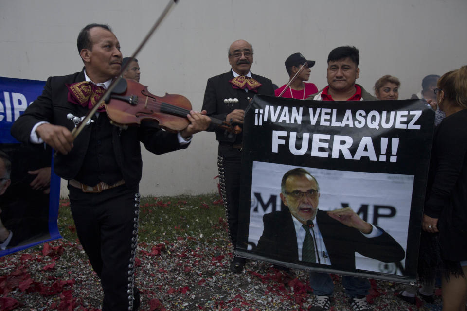 A mariachi plays his violin next to a man holding a banner with a message that reads in Spanish, "Get out Ivan Velasquez" and an image of Velasquez, head of a U.N.-sponsored anti-graft commission, during a protest outside the United Nations International Commission Against Impunity, CICIG, headquarters in Guatemala City, Friday, Aug. 31, 2018. Guatemalan President Jimmy Morales announced that he is shutting down the commission that pressed a number of high-profile corruption probes, including one pending against the president himself over purported illicit campaign financing. (AP Photo/Moises Castillo)