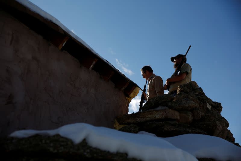 Drew Miller and Kacey Dawson stand on a lookout perch holding weapons at a survival camp