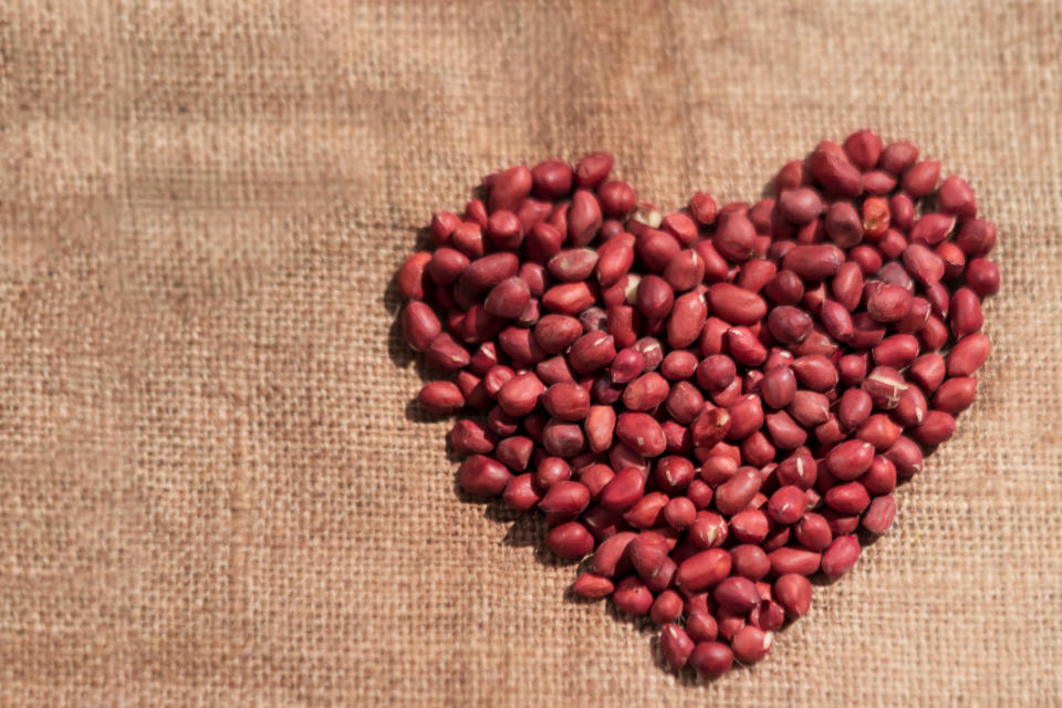 Raw unpeeled peanuts forming a heart shape defying a healthy heart on a burlap or sack cloth with copy space. Background photo for good healthy life.