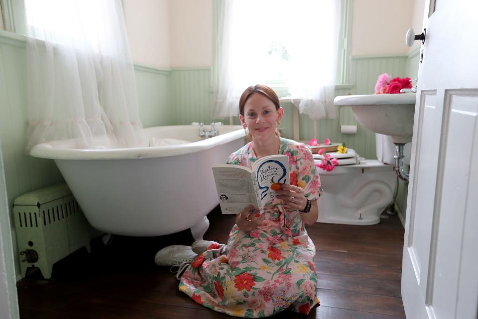 Janie Bragg, director of Flannery O'Connor Childhood Home & Foundation, sits with a book on the floor of the bathroom on the 2nd floor of the Flannery O'Connor Childhood Home. The bathroom was young Flannery's favorite place to find quiet in the home, often sitting in the porcelain tub.