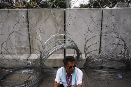 An anti-government protester sits near barbwire and barricades as demonstrators rally inside a compound of the Thai Royal Police Club in Bangkok February 21, 2014. REUTERS/Athit Perawongmetha