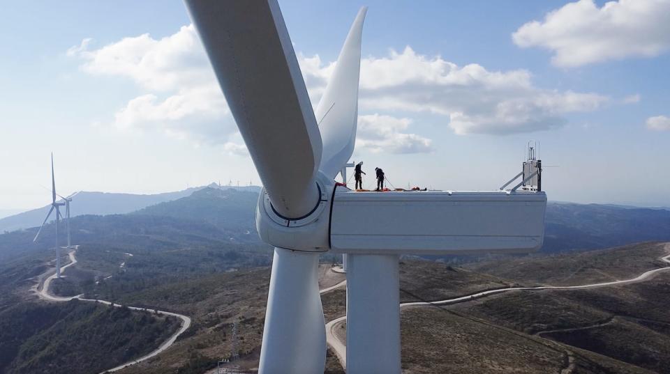 Two Wind turbine technicians on top of a wind turbine with mountains in the background.