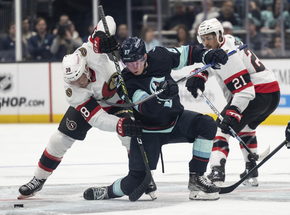 Seattle Kraken forward Morgan Geekie, center, works against Ottawa Senators forward Patrick Brown and forward Mathieu Joseph, right, for the puck during the first period of an NHL hockey game Thursday, March 9, 2023, in Seattle. (AP Photo/Stephen Brashear)