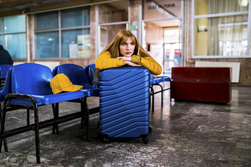 Young woman with suitcase sitting bored wait a time for traveler trip at train station