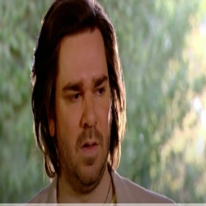 Matt Berry looks toward an audience with trees behind him