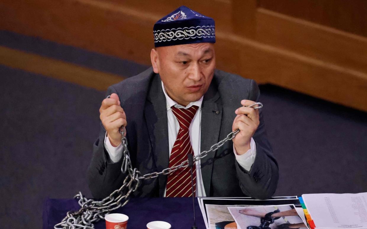 Witness Kazakh-Uyghur Omir Bekali demonstrates how he says he was shackled in chains at a re-education camp as he speaks on the first day of hearings at the "Uyghur Tribunal", a panel of UK-based lawyers and rights experts investigating alleged abuses against Uyghurs in China, in London on June 4, 2021. - The panel, which has no state backing, will begin hearing evidence from witnesses on Friday, and plans to issue a verdict on whether Beijing has perpetrated genocide or crimes against humanity against Uyghurs and other Muslim groups in China. Beijing has branded it a "machine producing lies". - Tolga Akmen/AFP via Getty Images 