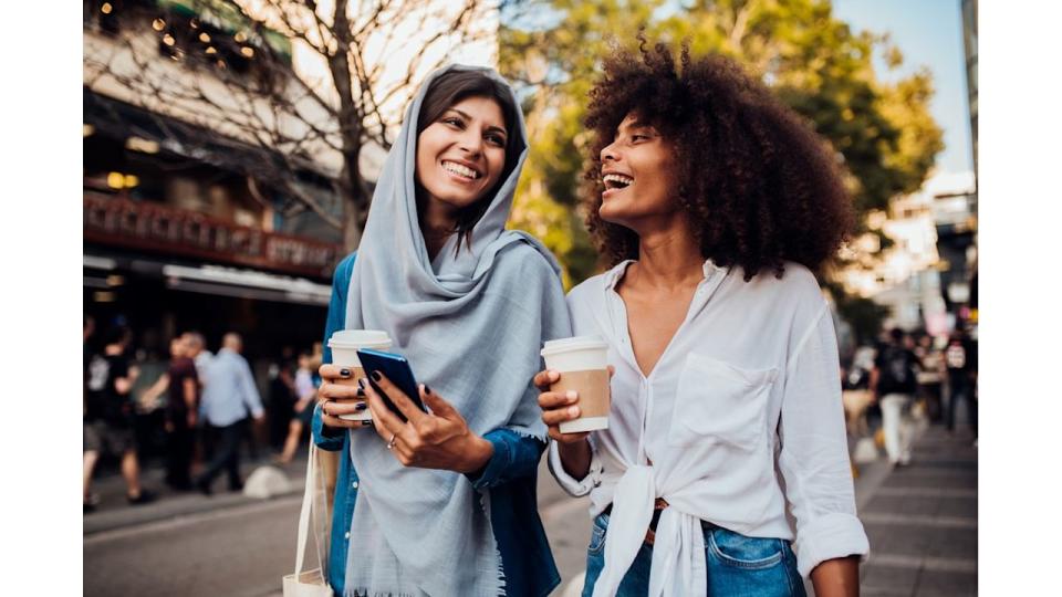 Portrait of two beautiful girls drinking coffee and surfing the net at the street.