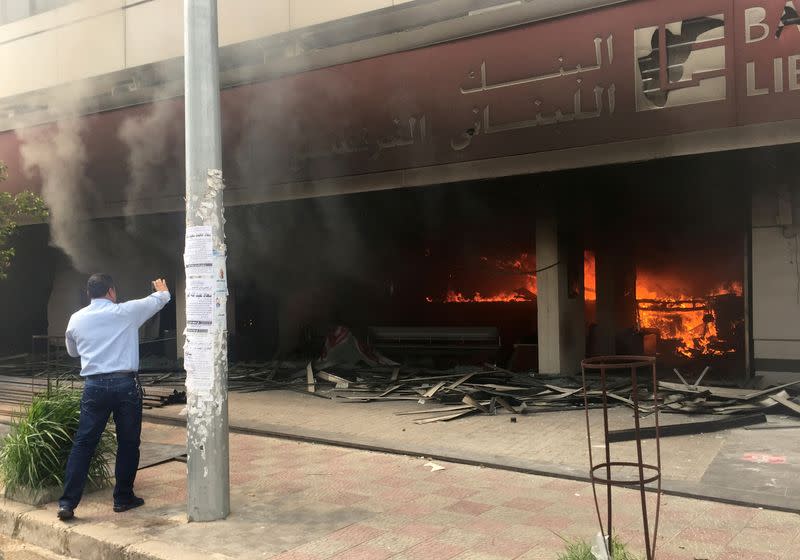 Man takes a picture with his mobile phone of a bank on fire during unrest in Tripoli