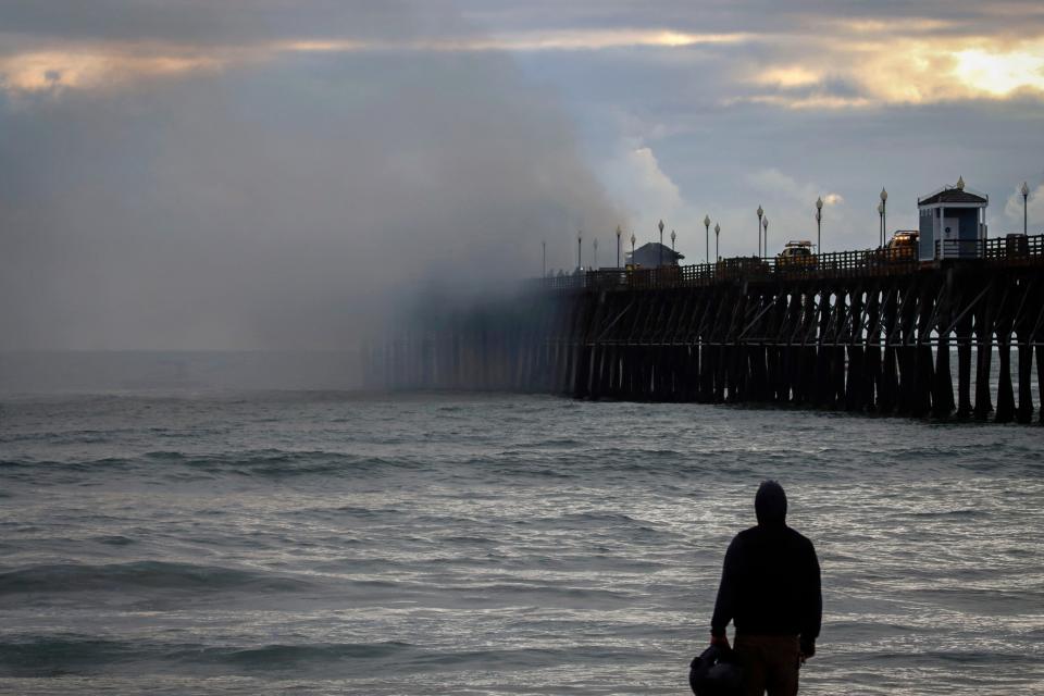 A beachgoer looks on from the shore as a massive fire burns on the West end of the Oceanside Pier.