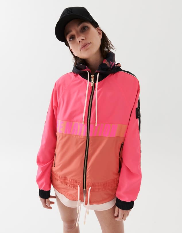 A model wears a pink colour blocked zip P.E Nations's Man Down Jacket over white shorts with a black hat.