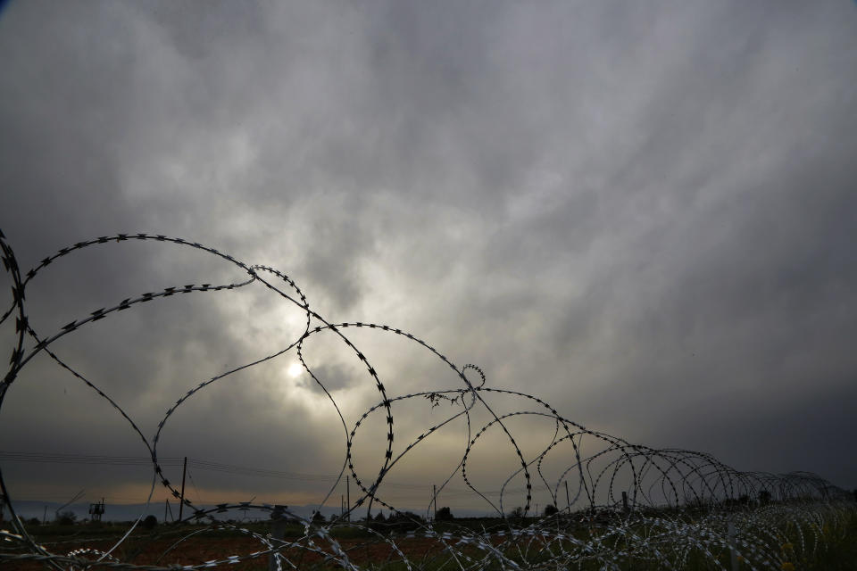 A Cypriot military guard post is seen at left behind razor wire along the southern side of a U.N buffer zone that cuts across the ethnically divided Cyprus during sunset near village of Astromeritis, Tuesday, March 9, 2021. The government of ethnically split Cyprus has come under fire over a decision to lay razor wire along a section of a U.N. controlled buffer zone it said is needed to stem migrant inflows from the island's breakaway north, with critics charging that the "ineffective" scheme only feeds partitionist perceptions amid a renewed push resume dormant peace talks. (AP Photo/Petros Karadjias)