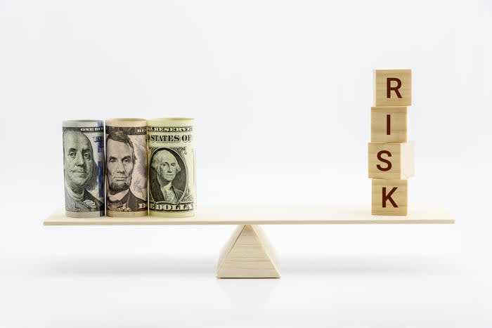 A wooden scale with cash on one side and blocks spelling out the word Risk on the other.