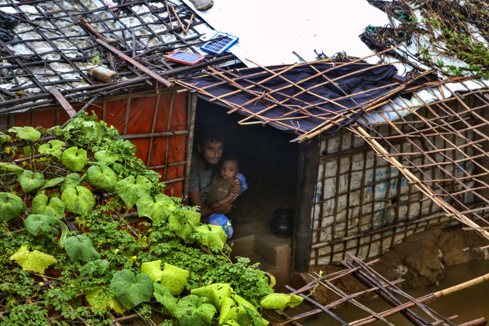 A Rohingya refugee man sits with his child inside his inundated shelter following heavy rains at the Rohingya refugee camp in Kutupalong, Bangladesh, Wednesday, July 28, 2021. Days of heavy rains have brought thousands of shelters in various Rohingya refugee camps in Southern Bangladesh under water, rendering thousands of refugees homeless. (AP Photo/ Shafiqur Rahman)