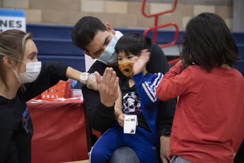 ARLETA, CA - NOVEMBER 08: Ocean Williams (cq), 5, high-fives his dad Aidan after getting the COVID-19 vaccine from nurse Chelsea Meyer, left, at Arleta High School on Monday, Nov. 8, 2021. Following the recent Centers for Disease Control and Prevention's approval of Pfizer's COVID-19 vaccine for children ages 5 to 11, Los Angeles Unified will offer voluntary vaccine access to students. The district highly encourages the vaccine for children ages 5 to 11, however, it will not be part of Los Angeles Unified's current student vaccine requirement. (Myung J. Chun / Los Angeles Times)