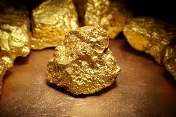 A gold nugget sitting on a surface with gold nuggets lined up behind it in a circle.