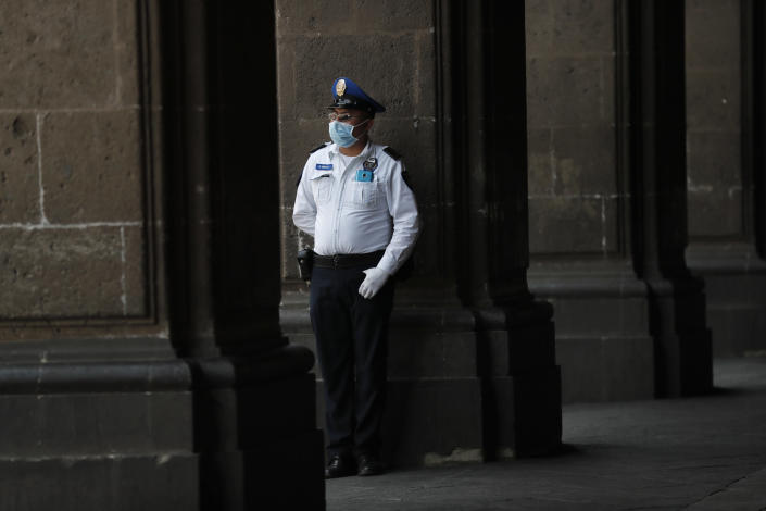 A police officer wearing protective gear against the spread of the new coronavirus, stands guard outside the mayor's office, in the historic center of Mexico City, Wednesday, April 1, 2020, where many businesses have temporarily closed. Mexico's government has broadened its shutdown of "non essential activities," and prohibited gatherings of more than 50 people as a way to help slow down the spread of COVID-19. (AP Photo/Marco Ugarte)
