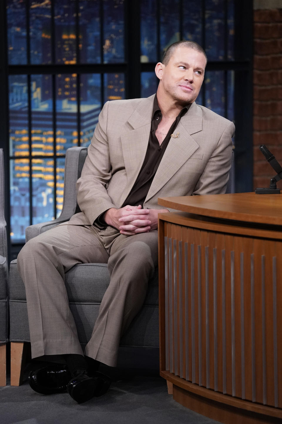 Channing Tatum sits on the set of a talk show wearing a light suit and black shoes