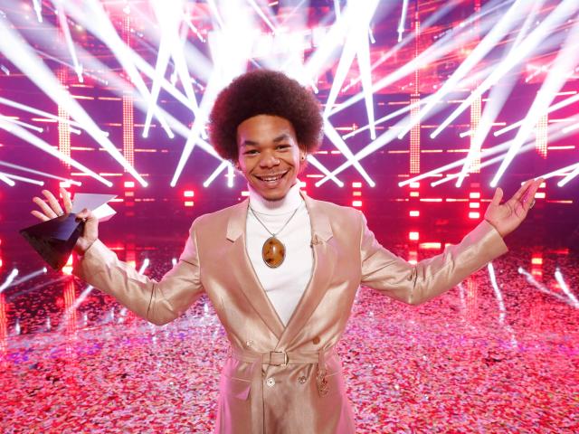 Cam Anthony holding his winning trophy in front of a red, strobe-light background on &quot;The Voice&quot;