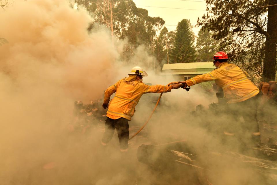 Firefighters hose down a burning woodpile during a bushfire in Werombi, 50km southwest of Sydney