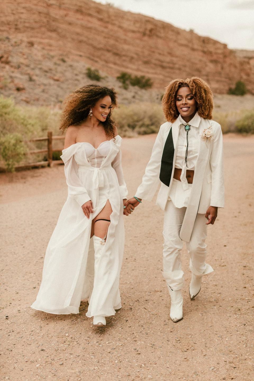 Two brides hold hands and walk in their wedding attire,