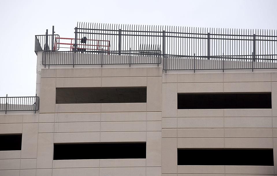 A barrier with a curved top to prevent people from climbing over is being installed around the ninth floor of the Fifth and Walnut municipal parking garage.