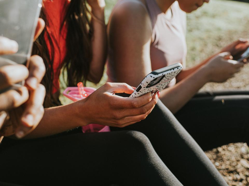 three women sitting on grass looking at phones