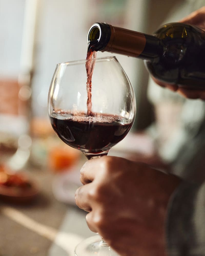 Man pouring red wine into a glass in dining room.