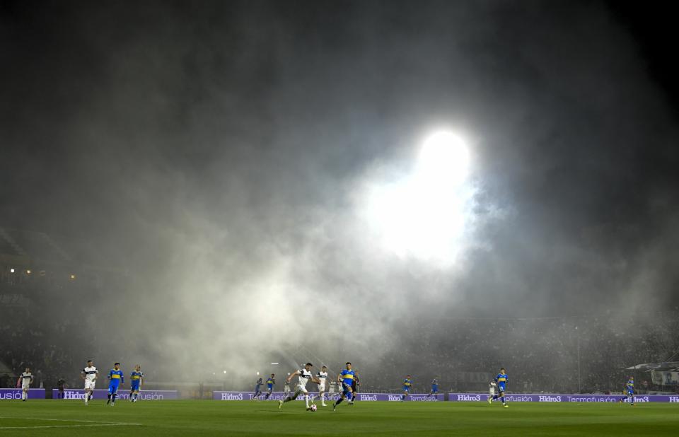 Players of Gimnasia de La Plata and Boca Juniors run after the ball as tear gas invades the field in La Plata, Argentina, Thursday, Oct. 6, 2022. The match was suspended after tear gas thrown by the police outside the stadium wafted inside affecting the players as well as fans who fled to the field to avoid its effects. (AP Photo/Gustavo Garello)