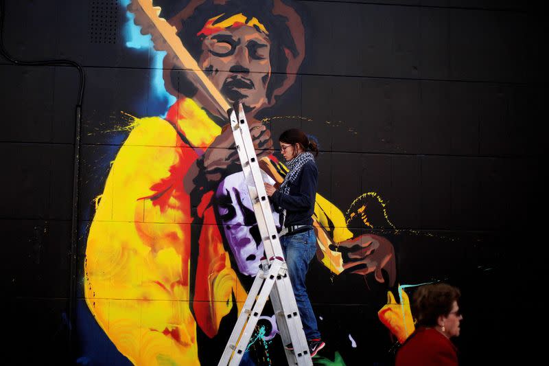 FILE PHOTO: A woman paints graffiti of the rock star Jimi Hendrix, on the wall of a music shop in Malaga