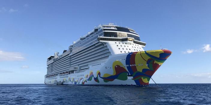 A Norwegian Cruise Lines ship with a colourful side sets sail on a sunny day.