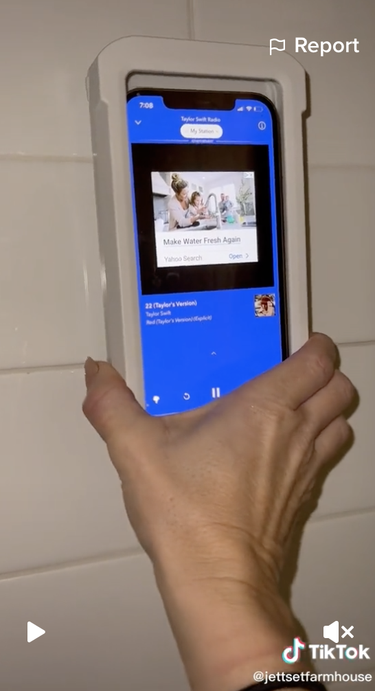 A woman's hand holds a phone in amazon waterproof phone holder against a tiled shower wall.