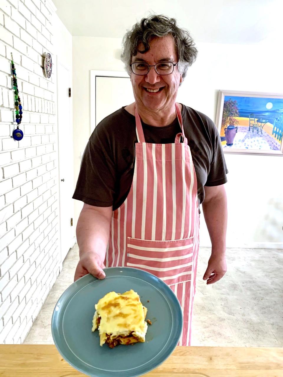 Greek dad proudly holding a plate of his pastitio