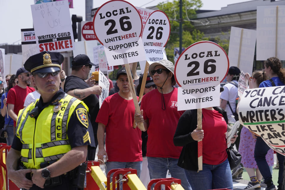 Protesters supporting the Hollywood writers' strike march past a member of law enforcement, left, while forming a picket line outside an entrance to Boston University commencement ceremonies, Sunday, May 21, 2023, in Boston. David Zaslav, president and CEO of Warner Bros. Discovery, delivered an address during ceremonies Sunday. (AP Photo/Steven Senne)