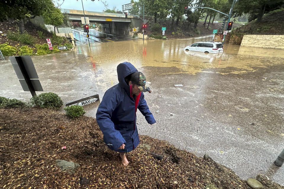 A pedestrian tries to walk around a flooded zone near an overpass as rain comes down, Thursday, Dec. 21, 2023, in Santa Barbara, Calif. (AP Photo/Eugene Garcia)