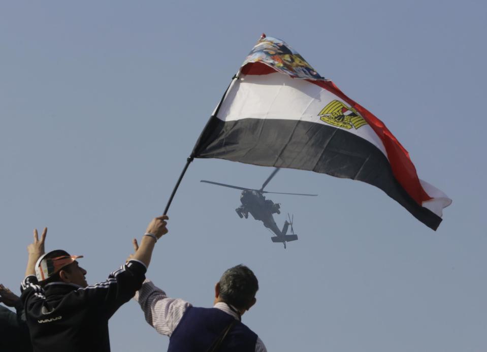 Egyptians wave a national flag as they greet an army helicopter flying over Tahrir Square, the epicenter of the 2011 uprising, in Cairo, Egypt, Saturday, Jan. 25, 2014. As Egyptians mark the third anniversary of their spectacular revolt against autocrat Hosni Mubarak in the name of democracy on Saturday, there has been a powerful sign of the country's stunning reversals since: letters of despair by some of the prominent activists who helped lead the uprising, leaked from the prisons where they are now jailed. (AP Photo/Amr Nabil)